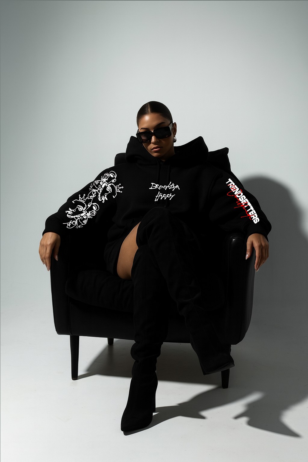 BKLYN HIPPY campaign: model seated in a black armchair wearing a black BKLYN HIPPY hoodie